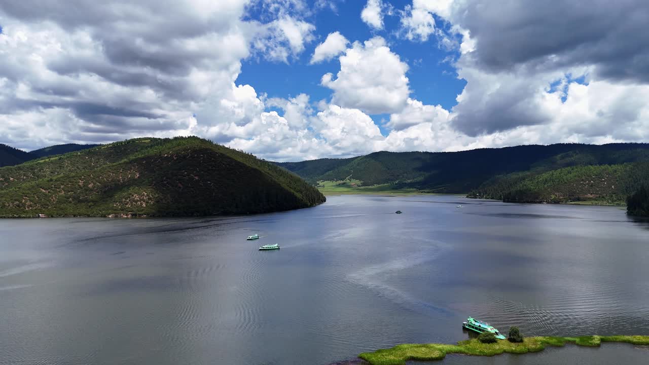 Panorâmica aérea de um lago alpino cercado por montanhas verdes com barcos e reflexos de nuvens, Parque Nacional Potatso Shangri-la Yunnan China
