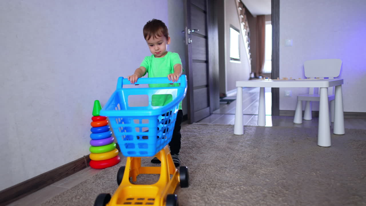 Little kid enters his room pushing a toy shopping cart. Lovely baby boy playing at home.