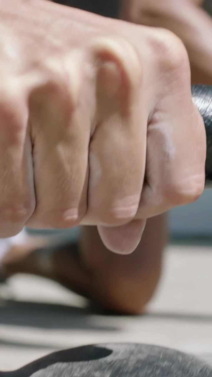 Vertical video: Chalking hands, man in shirt kneeling mat, gripping kettlebell preparing lift