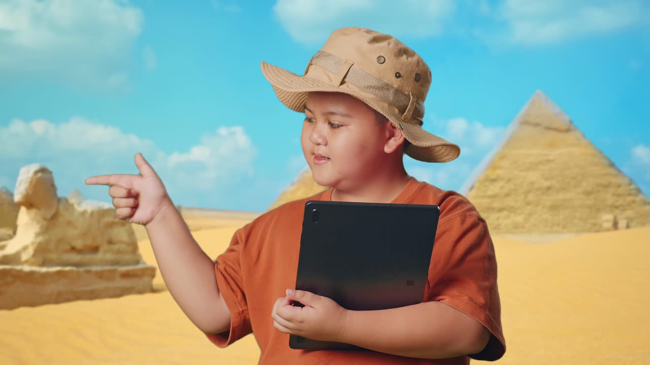 Asian Boy With A Hat And Binoculars Using A Tablet Then Smiling And Pointing To Side While Traveling In Giza Pyramid. Boy Researcher Examines Something, Travel Adventure Concept, Close Up