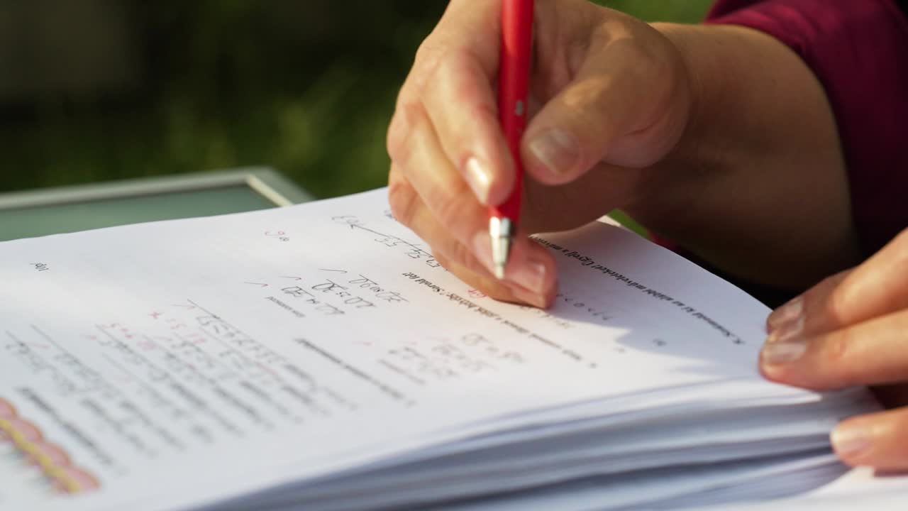 Close-up of hands holding a red pen while reviewing papers outdoors