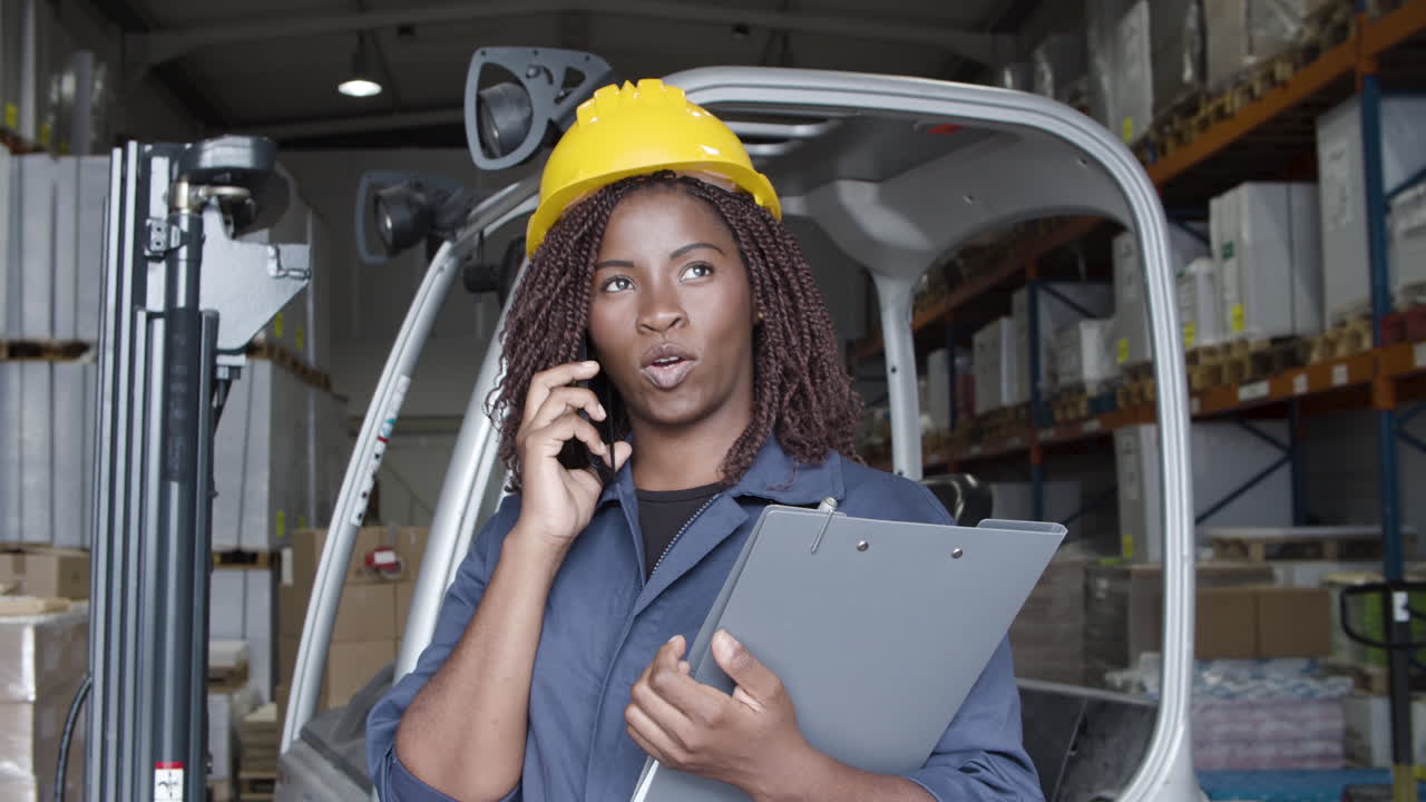 African American female worker talking on phone, standing in storehouse and holding a clipboard