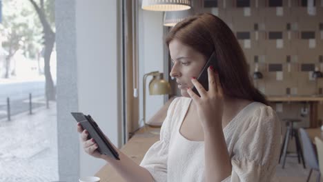 una mujer muy joven y seria hablando por celular mientras sostiene una tableta