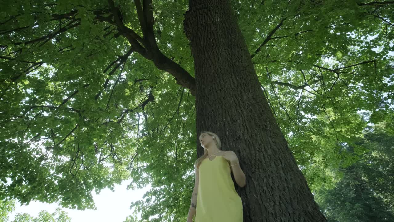 mujer con vestido amarillo bailando junto al árbol en el parque de verano