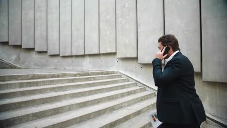 business man with documents walking up stairs. male worker talking on smartphone