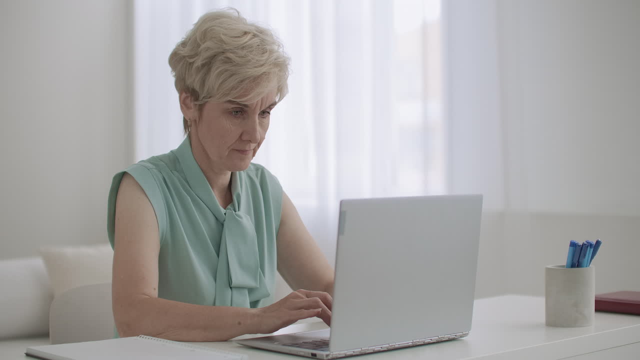 aged woman is working remotely using laptop with internet connection for communicating typing message in online chat