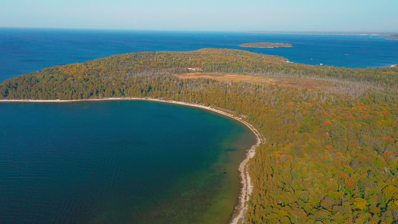 The Door County peninsula stretches between emerald shallows and deep blue lake water, where autumn forests meet the calm horizon of Lake Michigan under clear skies