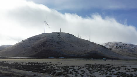 Una-Carretera-Ensombrecida-Por-Altas-Turbinas-De-Viento-En-Una-Ladera-En-Invierno-En-Un-Día-Nublado