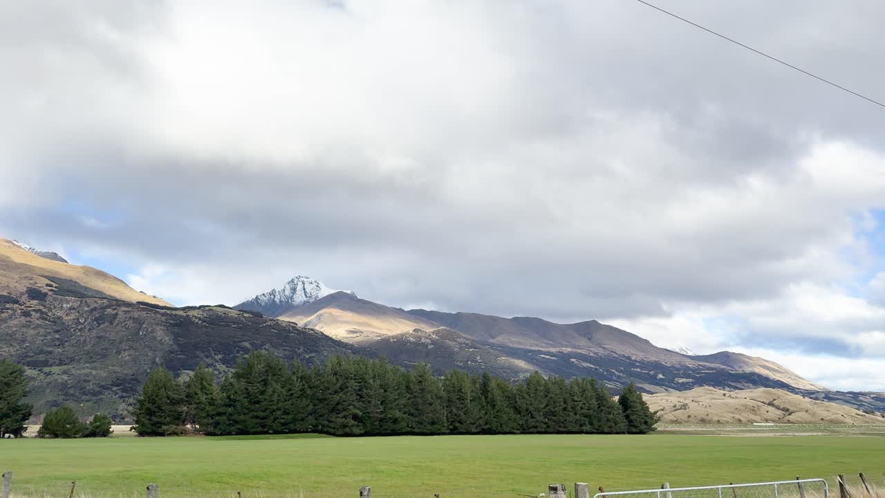 Camera pans across Mount Earnslaw, green fields, and forest under bright, partly cloudy daylight