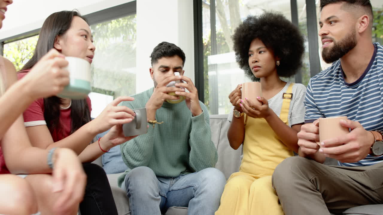 Young friends sitting on couch, drinking coffee, and having conversation