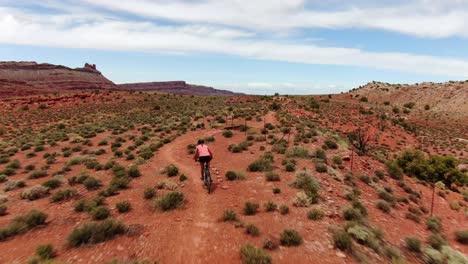 Toma-Aérea-Siguiendo-A-Una-Mujer-Montando-En-Bicicleta-De-Montaña-A-Lo-Largo-Del-Hermoso-Sendero-Remoto-De-Moab