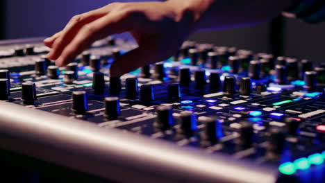 a hand adjusting controls on a professional sound mixer with colorful lights