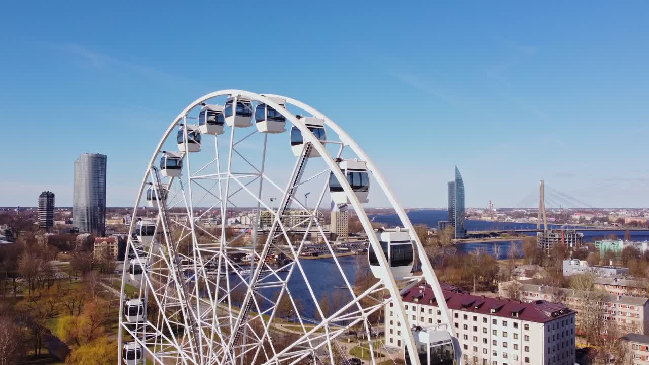 Ferris wheel near Daugava River with Riga skyline and modern city buildings