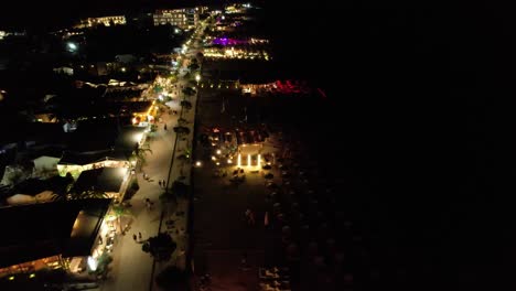 beach bars aglow with lights, waves gently lapping the dark sea, evoking joyful summer vacation vibes by night in dhermi