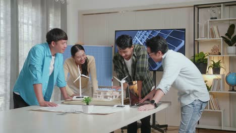 un grupo de ingenieros asiáticos celebra el final del ensamblaje del modelo de casas pequeñas con panel solar en la oficina