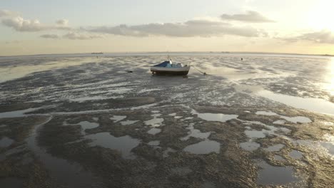 Lonely-boat-stranded-on-mud-with-warming-sunset-and-sun-flare-on-Southend-beach-in-Essex,-UK