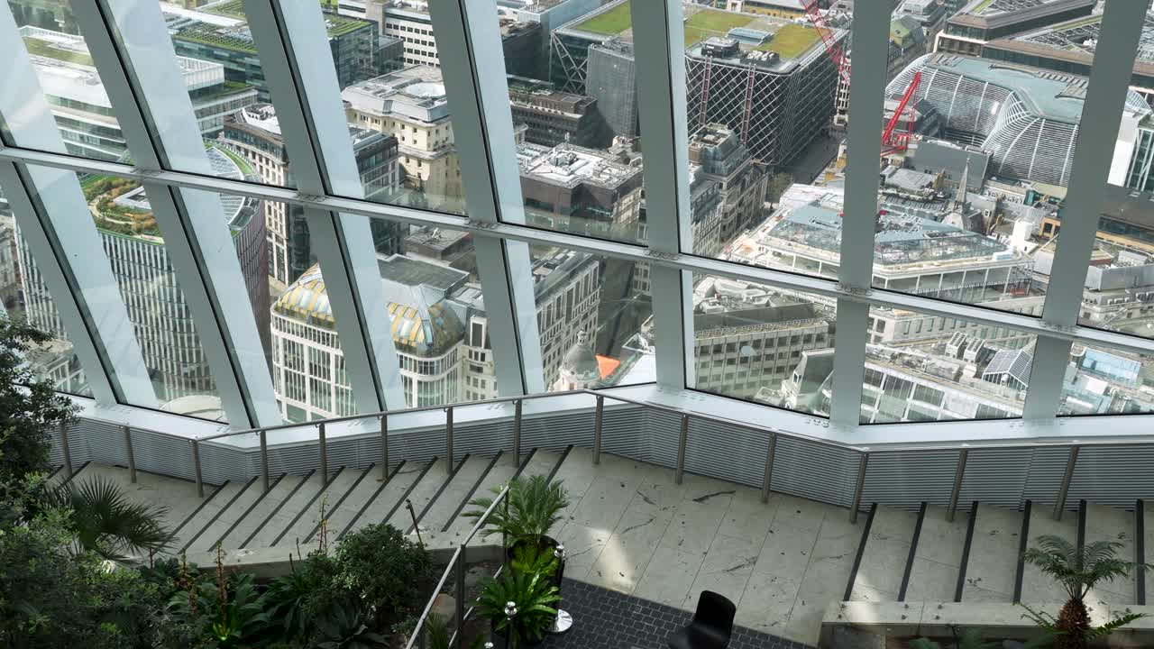 Vista desde el Sky Garden en Londres mirando hacia los edificios de la ciudad a través de grandes ventanales. Escena interior con plantas y escaleras con vistas al paisaje urbano