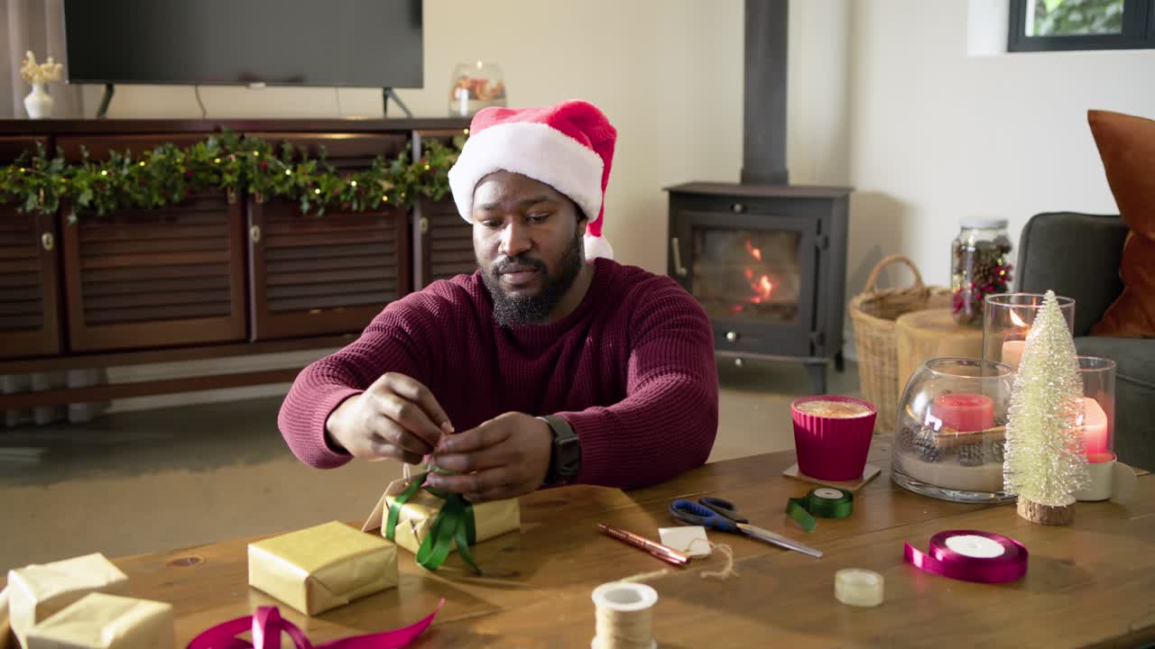 Inspired by holiday cheer, African American man tying green ribbon to gold gift box at home