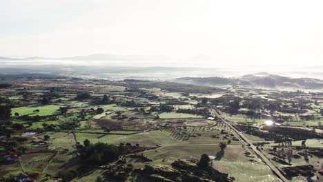 Drone-shot-of-sun-drenched-hilly-landscape-with-plantations,-fields-and-trees