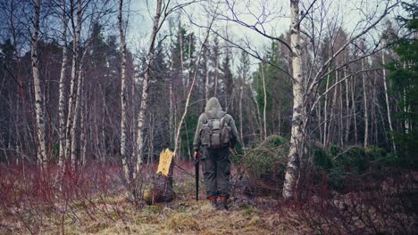 a man with a backpack holding a hand saw and an axe. static shot