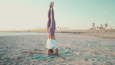 una chica yogui de pie en la cabeza haciendo posturas de yoga junto al mar.