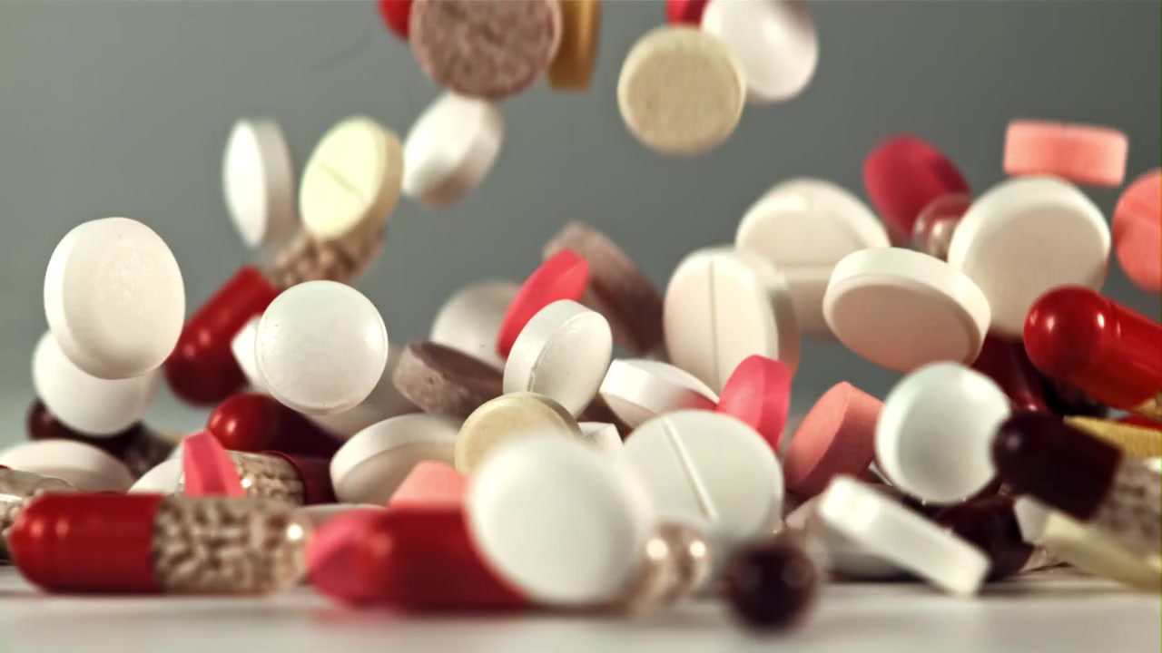 Various Colorful Pills and Capsules Falling onto a White Surface in Slow Motion