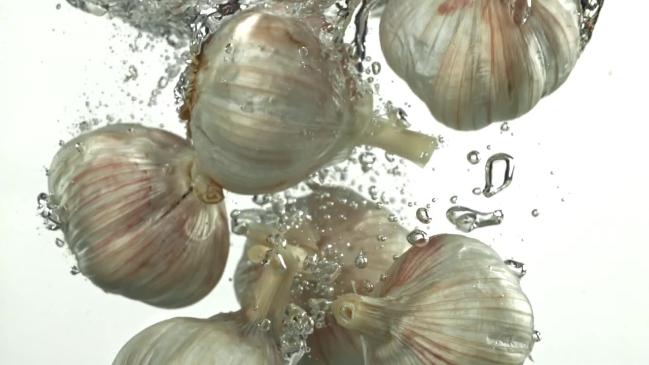 Bulbi d'aglio freschi che cadono nell'acqua con bolle al rallentatore.