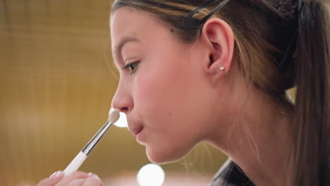 vista de primer plano de una mujer tocando el polvo en su cara usando un pincel de maquillaje, aplicando el pó al rostro con cuidado, centrándose en la técnica de maquillajes, rutina de belleza, aplicación de maquillajen facial cercana