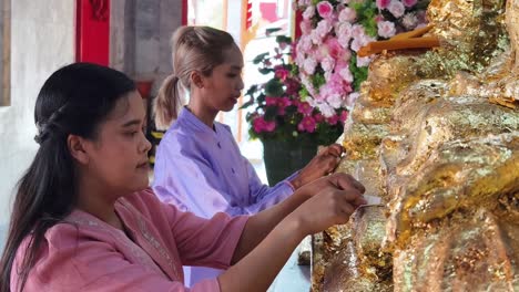 thai women praying and applying gold leaf at a temple