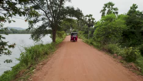 a red tuk-tuk drives down a dirt road surrounded by lush greenery and palm trees in sri lanka