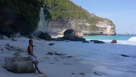 Young-woman-enjoys-the-big-waves-rolling-out-of-the-blue-water-at-Suwehan-Beach-in-Indonesia-on-a-sunny-day