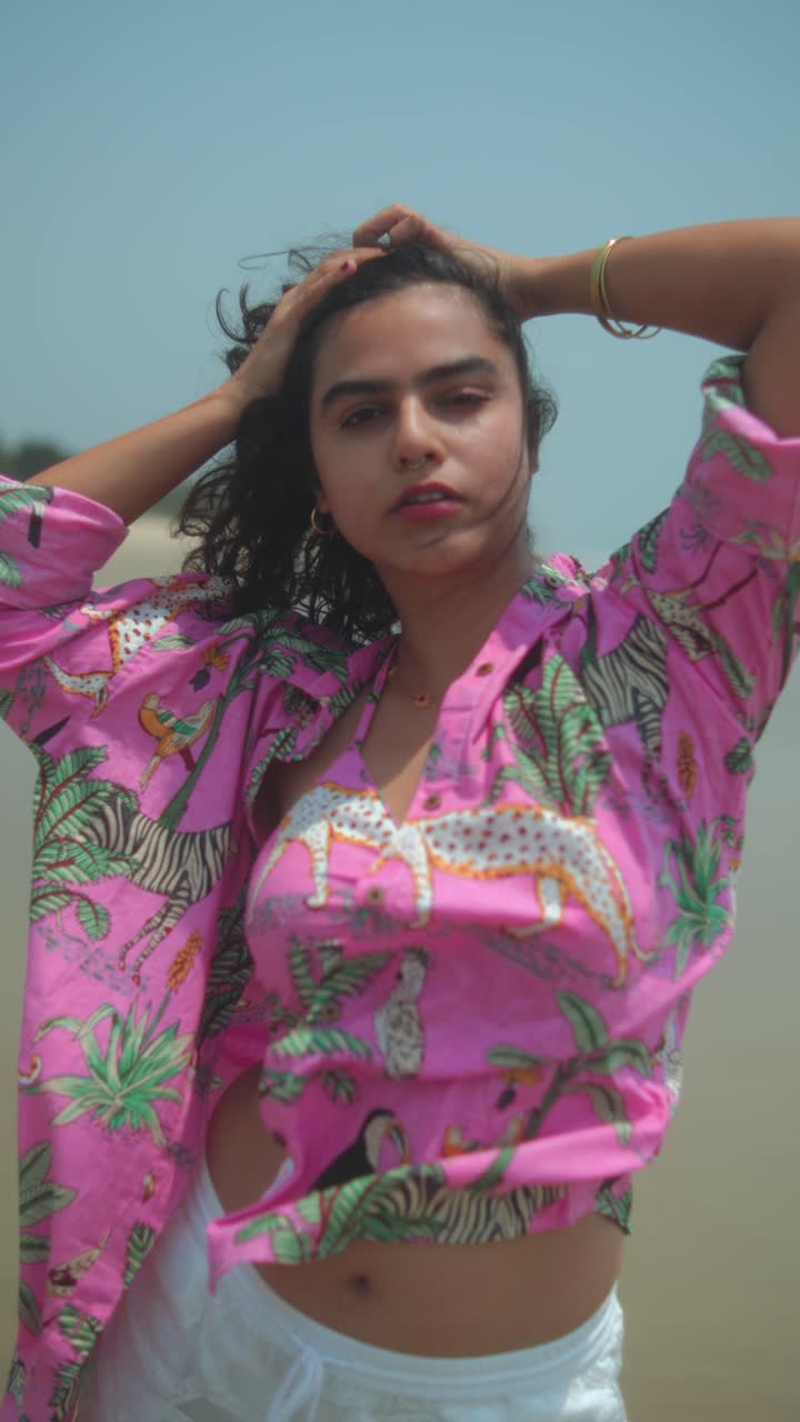 Young woman in pink shirt posing gracefully on a quiet beach in warm daylight