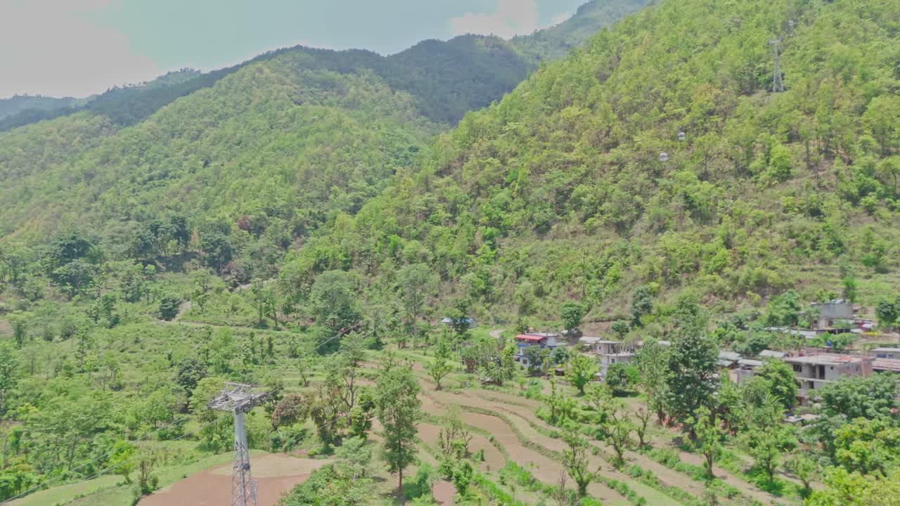 A cable car moves smoothly across a lush green mountain landscape, offering a scenic view of nature and hillside terrain. Ideal footage for travel, tourism, transportation, and eco-adventure themes