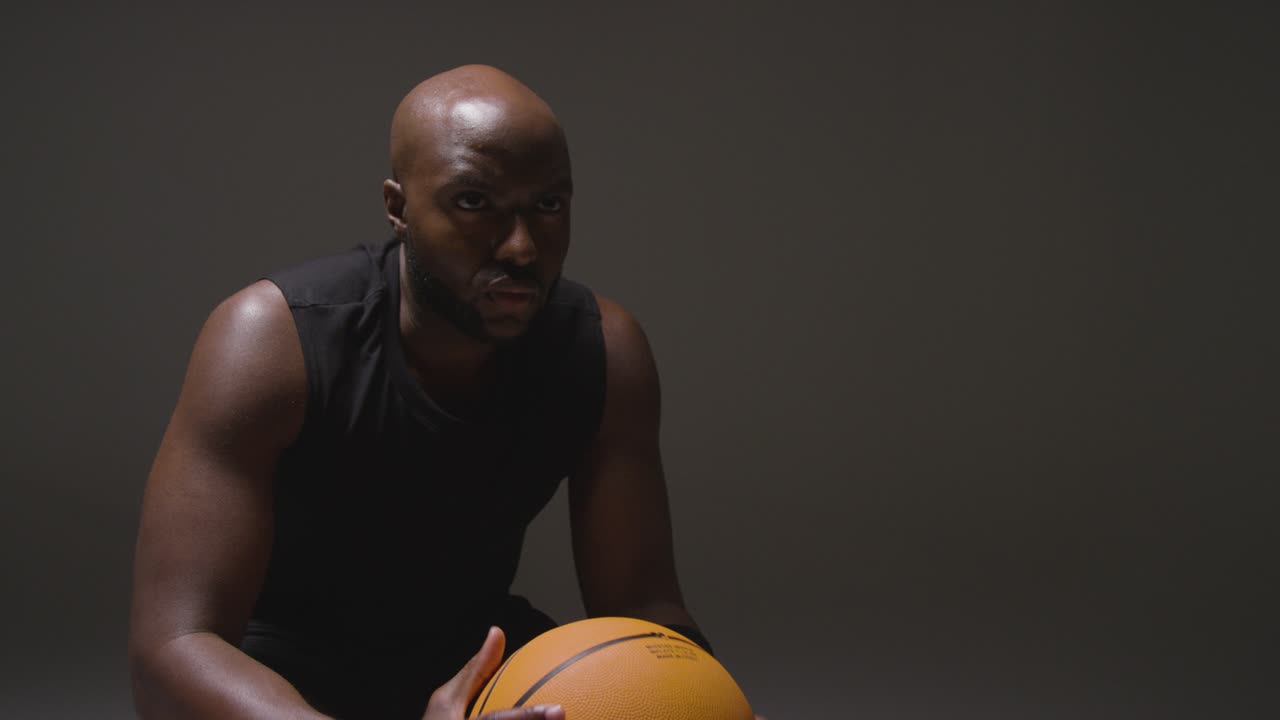 Studio Shot Of Seated Male Basketball Player With Hands Holding Ball 2