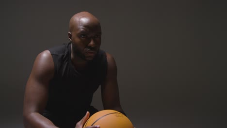 studio shot of seated male basketball player with hands holding ball 2