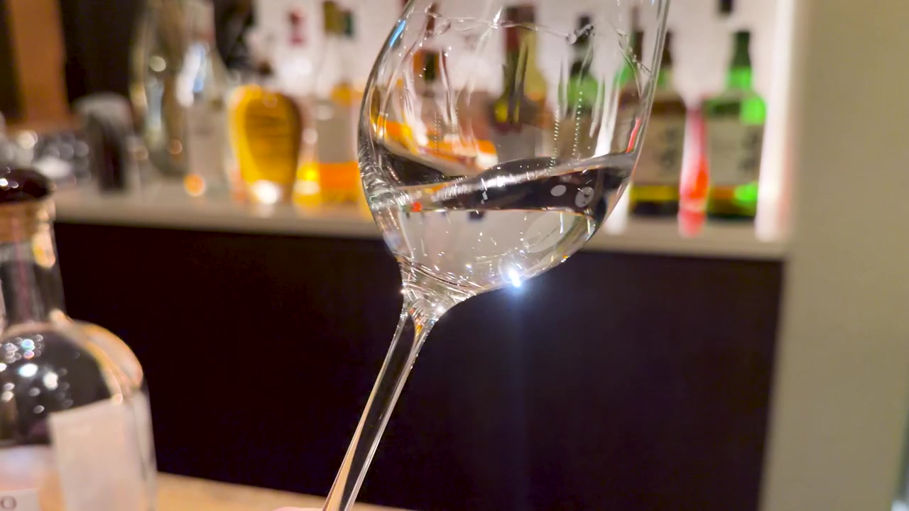 Close-up de saquê transparente girando dentro de uma taça de vinho em um bar com pouca luz