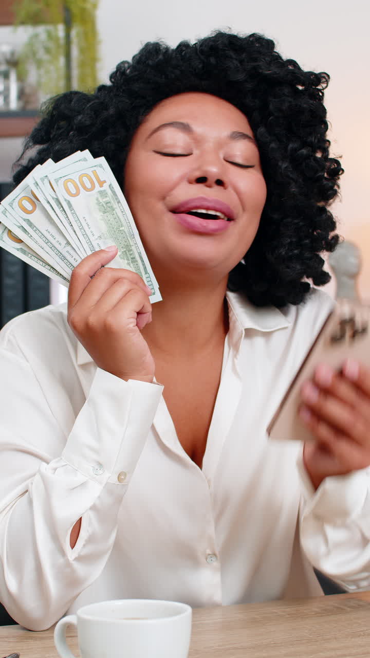 Felice donna d'affari afroamericana che tiene in mano dollari e contanti, con uno smartphone festeggia un enorme budget di guadagni
