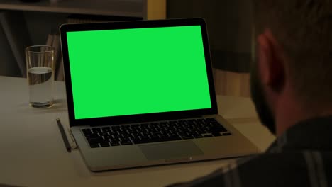 hombre navegando contenido en la computadora portátil con pantalla verde clave de croma mientras está sentado en la oficina de casa. joven utiliza la computadora para el trabajo remoto, la educación en línea o la comunicación en casa. cerca. cámara lenta