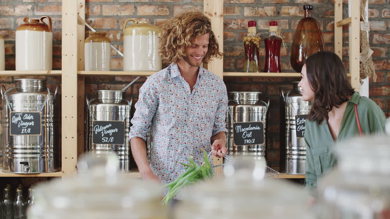 젊은 부부가 지속 가능한 플라스틱 없는 식료품 가게에서 신선한 과일과 채소를 구입하고 있습니다.