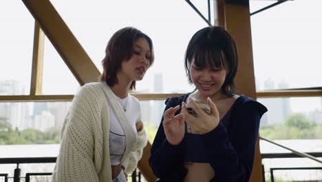 two young women socializing and looking at a smartphone outdoors