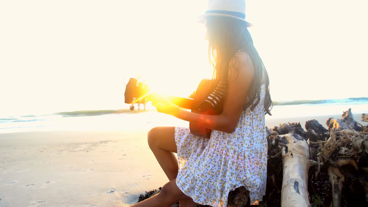 아시아인 여성이 해변에서 기타를 연주하고 노래하고 있습니다.