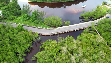 Drone-of-passing-vehicles-over-road-at-the-Port-launay-mangrove,-water-reflection,-tropical-forest-with-palm-trees-and-granite-stone,-Mahe-Seychelles-30fps