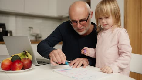 Grandfather-teach-granddaughter-drawing-and-doing-homework-at-home