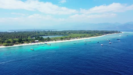 boats sailing around tropical island shore with white sandy beach and lush vegetation on a bright sunny day indonesia