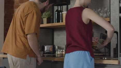 dos compañeros de cuarto limpiando la cocina y lavando la taza en un piso compartido