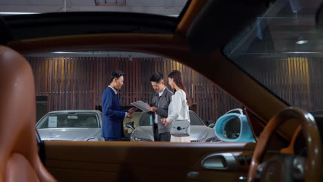 couple with attractive auto dealer in a suit presenting new car model to his client