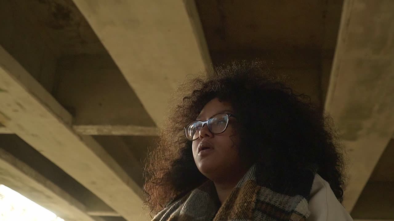 mujer negra con gafas y retrato de cabello rizado debajo de un puente