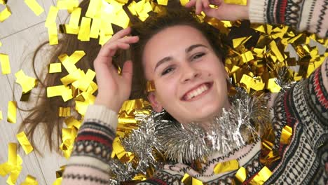 close up view of young happy smiling woman lying on the floor, the golden confetti falling on her. slow motion shot