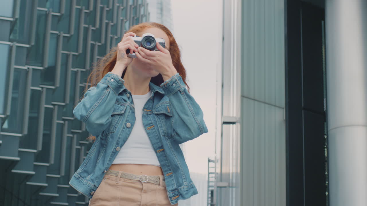 도시 에 있는 젊은 여성 이 소셜 미디어 에 게시 하기 위해 디지털 카메라 로 사진 을 찍고 있다