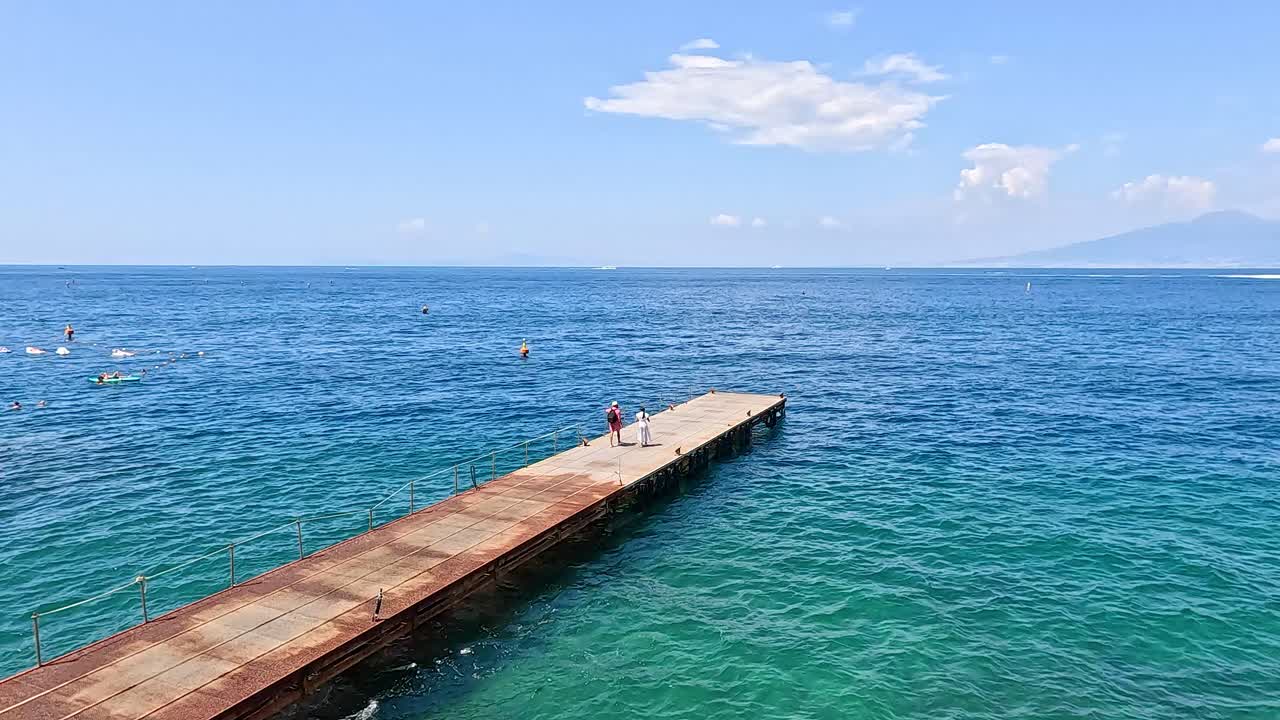Man walks on pier over clear blue water